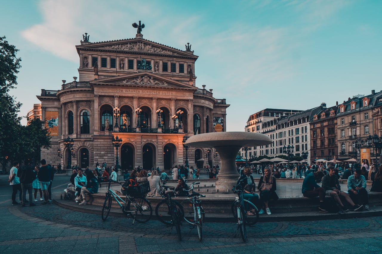 A vibrant urban scene with people relaxing around a fountain in front of a historic building at twilight.