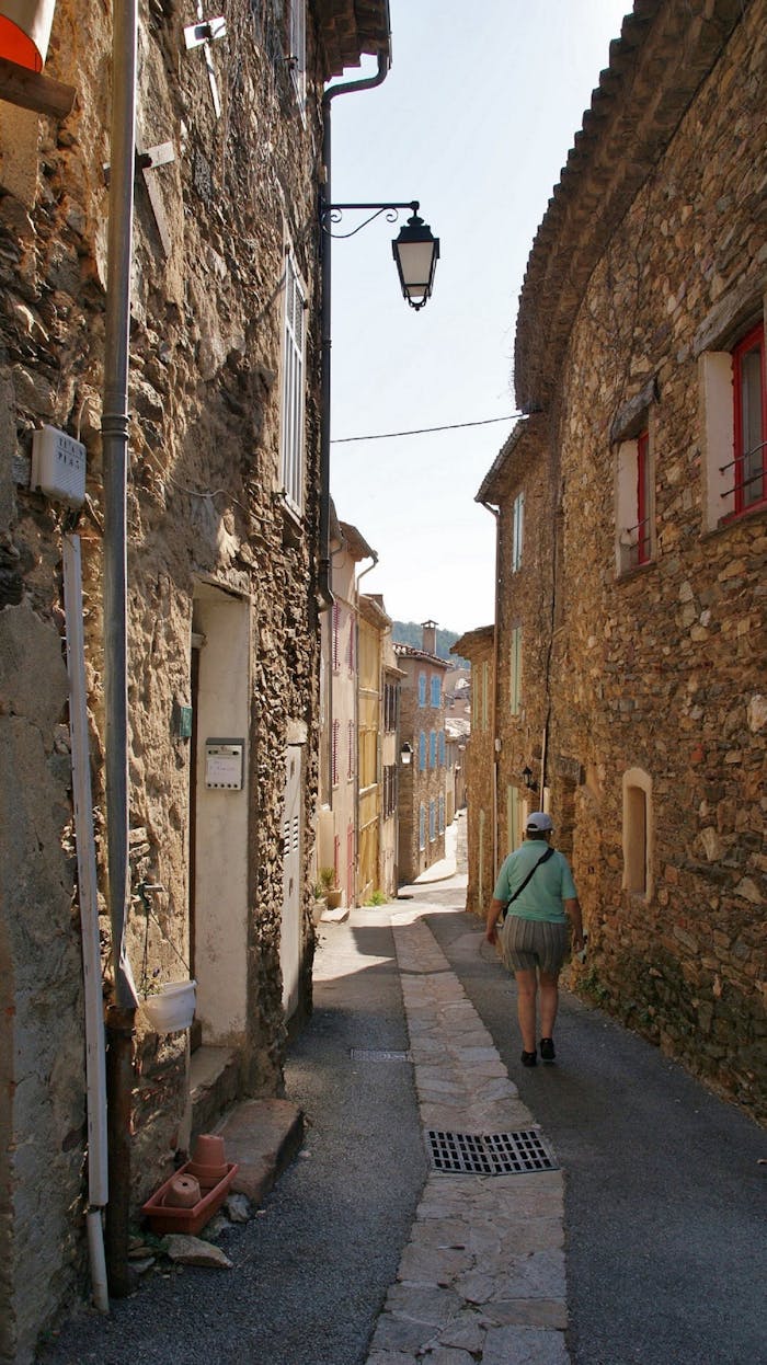 A person walking down a sunlit historic alleyway with rustic stone walls.